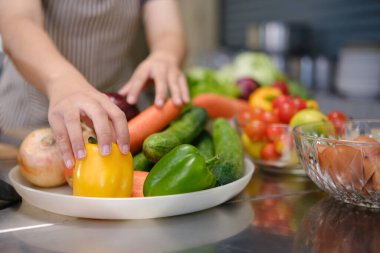 Aşçılık öğrencisi profesyonel bir eğitim mutfağında pratik ve öğrenme için hazırlanmış taze malzemelerle elleriyle yemek pişirmeye hazır bekliyor..