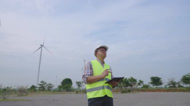 Rüzgâr türbini alanından geçen mühendis bulutlu gökyüzünün altında yenilenebilir enerji altyapısını inceliyor. Yüksek kalite 4k görüntü
