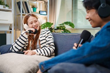 Genç adam ve kadın koltukta otururken mikrofon ve kulaklık kullanarak podcast yapıyorlar..