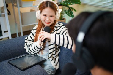 Evde podcast yaparken gülümseyen genç bir kadın. Kapalı alanda mikrofon ve kulaklık kullanıyor..