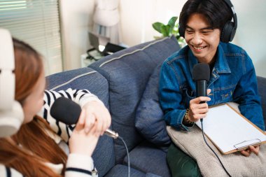 Genç adam kanepede yardımcı sunucuyla konuşurken mikrofon ve kulaklık kullanarak podcast yapıyor..