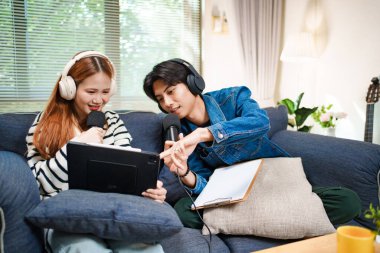 Genç adam ve kadın internet içeriği oluşturmak için kanepede otururken tablet ve mikrofon kullanarak podcast yapmayı planlıyorlar..