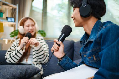 Genç adam kanepede yardımcı sunucuyla konuşurken mikrofon ve kulaklık kullanarak podcast yapıyor..