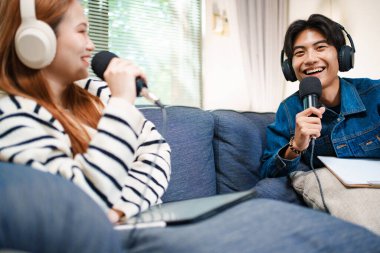 Genç adam kanepede yardımcı sunucuyla konuşurken mikrofon ve kulaklık kullanarak podcast yapıyor..