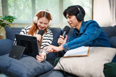 Genç adam ve kadın internet içeriği oluşturmak için kanepede otururken tablet ve mikrofon kullanarak podcast yapmayı planlıyorlar..