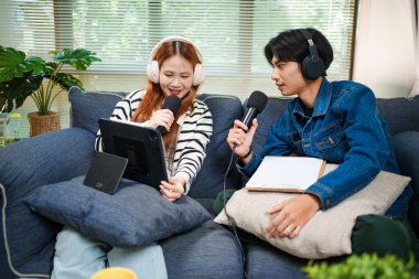 Genç adam ve kadın internet içeriği oluşturmak için kanepede otururken tablet ve mikrofon kullanarak podcast yapmayı planlıyorlar..