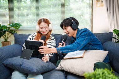 Genç adam ve kadın internet içeriği oluşturmak için kanepede otururken tablet ve mikrofon kullanarak podcast yapmayı planlıyorlar..