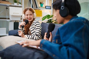 Genç adam ve kadın koltukta otururken mikrofon ve kulaklık kullanarak podcast yapıyorlar..