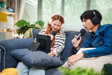 Genç adam ve kadın internet içeriği oluşturmak için kanepede otururken tablet ve mikrofon kullanarak podcast yapmayı planlıyorlar..