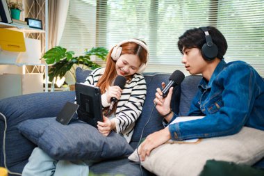 Genç adam ve kadın internet içeriği oluşturmak için kanepede otururken tablet ve mikrofon kullanarak podcast yapmayı planlıyorlar..