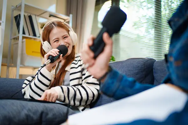 Genç adam ve kadın koltukta otururken mikrofon ve kulaklık kullanarak podcast yapıyorlar..