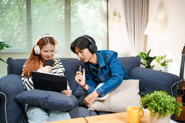 Genç adam ve kadın internet içeriği oluşturmak için kanepede otururken tablet ve mikrofon kullanarak podcast yapmayı planlıyorlar..