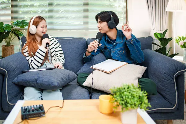 Genç adam ve kadın evlerinde kulaklık ve mikrofonla podcast yaparken masada ses mikseriyle oturuyorlar..