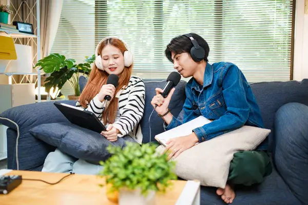 Genç adam ve kadın internet içeriği oluşturmak için kanepede otururken tablet ve mikrofon kullanarak podcast yapmayı planlıyorlar..