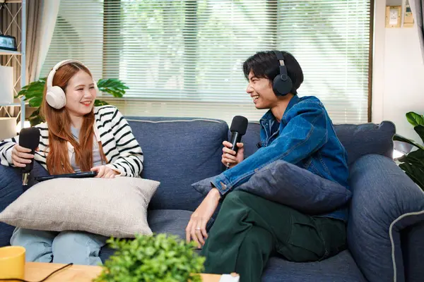 Genç adam ve kadın evlerinde kulaklık ve mikrofonla podcast yaparken masada ses mikseriyle oturuyorlar..