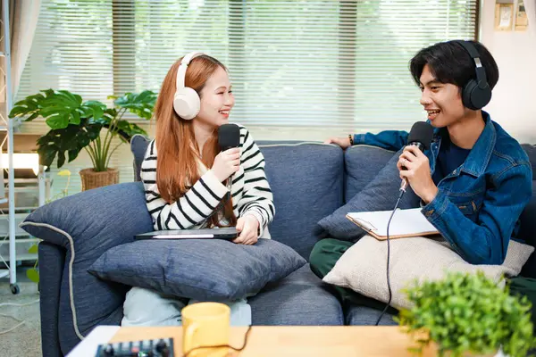 Genç adam ve kadın evlerinde kulaklık ve mikrofonla podcast yaparken masada ses mikseriyle oturuyorlar..