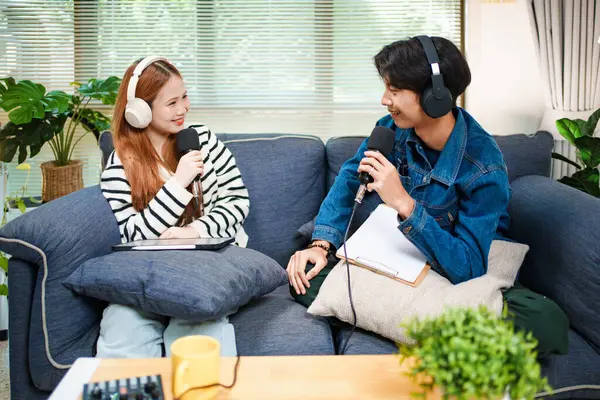 Genç adam ve kadın evlerinde kulaklık ve mikrofonla podcast yaparken masada ses mikseriyle oturuyorlar..