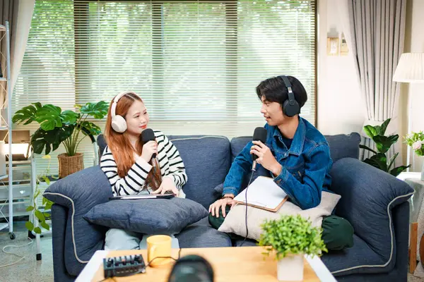 Genç adam ve kadın evlerinde kulaklık ve mikrofonla podcast yaparken masada ses mikseriyle oturuyorlar..