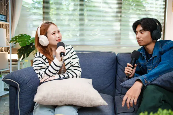 Genç adam ve kadın evlerinde kulaklık ve mikrofonla podcast yaparken masada ses mikseriyle oturuyorlar..