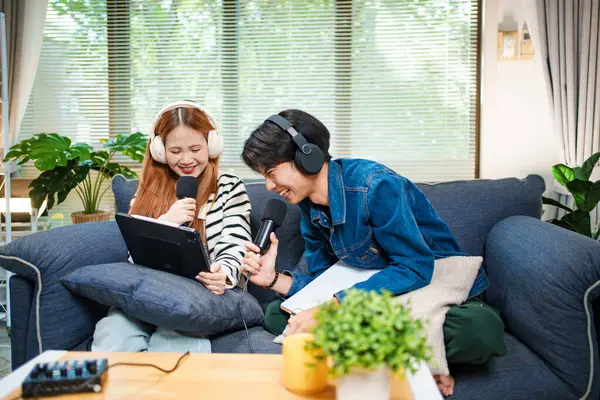 Genç adam ve kadın internet içeriği oluşturmak için kanepede otururken tablet ve mikrofon kullanarak podcast yapmayı planlıyorlar..