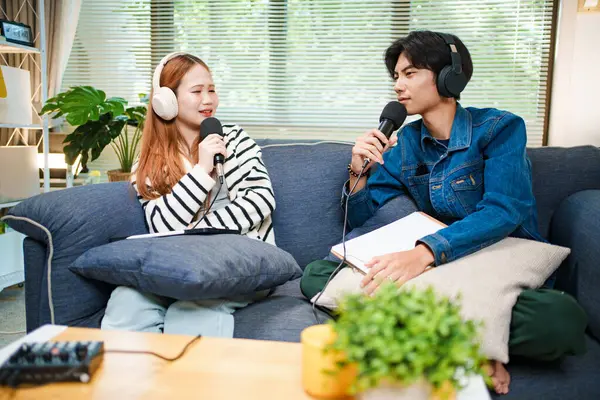 Genç adam ve kadın evlerinde kulaklık ve mikrofonla podcast yaparken masada ses mikseriyle oturuyorlar..