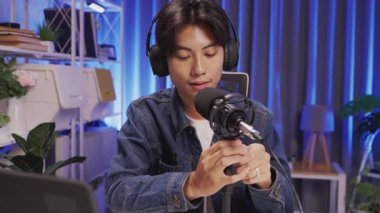 Kendine güvenen genç erkek içerik yaratıcısı kayıt sırasında yaratıcı mavi ışıklı ev stüdyosunda podcast mikrofonu ayarlıyor