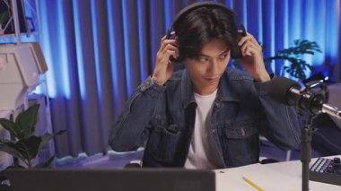 Kulaklık takan, canlı yayın ya da podcast 'e başlayan kendine güvenen genç adam, mavi ışıklı yaratıcı ev stüdyosunda mikrofona konuşuyor.