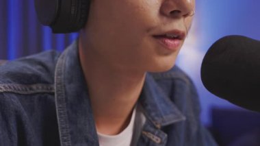 Bir ev stüdyosunda canlı yayın veya ses kaydı sırasında podcast mikrofona konuşan genç bir Asyalı içerik yaratıcısının ayrıntılı görüntüsü