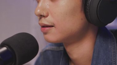 Sessiz bir ev stüdyosunda podcast ya da canlı yayın sırasında sakin bir şekilde profesyonel bir mikrofona konuşan Asyalı genç etkileyicinin aşırı yakın çekimi.