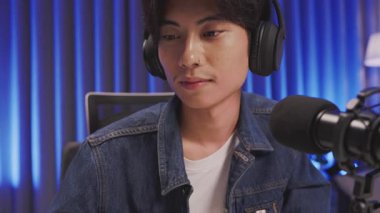 Modern bir ev stüdyosunda podcast ya da canlı yayın sırasında mikrofona konuşurken konsantre olan genç Asyalı erkek etkili.