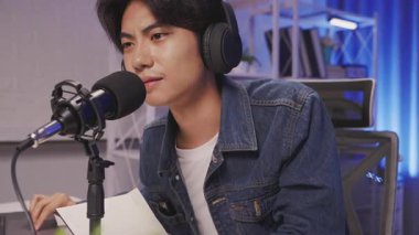 Sessiz ve odaklanmış bir ev stüdyosunda podcast mikrofona konuşan genç Asyalı içerik yaratıcısı