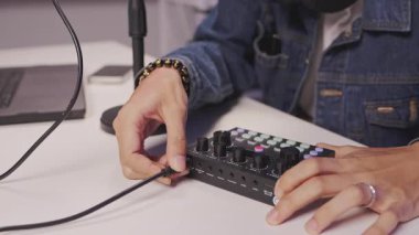 Podcast ya da canlı yayın kaydına hazırlanırken ses karıştırıcının kablo ve ayar kontrol düğmelerini bağlayan genç bir adamın ayrıntılı görüntüsü