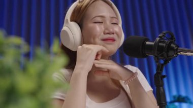 Canlı yayında seyirciyle uğraşırken podcast sunucusu gülümsüyor, modern stüdyoda yan açıyla çekiliyor..