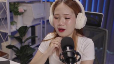 Kadın podcast sunucuları mikrofona konuşurken, modern ev stüdyosunda canlı yayında seyircilerle iletişim kuruyor.