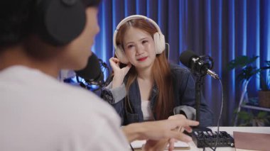 Bir podcast konuğu, omuzlarının üzerinden gösterilen canlı kayıt sırasında gülümser ve dikkatle ev sahibini dinler.