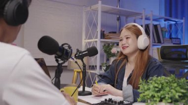 Bir bayan konuk, podcast sunucusunu dikkatle dinliyor. İlgi ve bağlantıyı yansıtıyor..