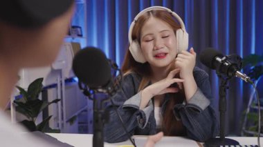 Bir podcast sunucusu canlı bir röportaj sırasında bir misafirle meşgul olurken gülümseyerek dinler..