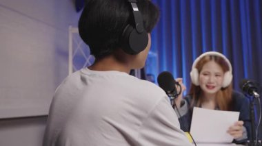 Podcast röportajında konuşan bir konuğun omuzlarının üzerinden sunucuyla masadaki canlı etkileşimi gösteriyor..