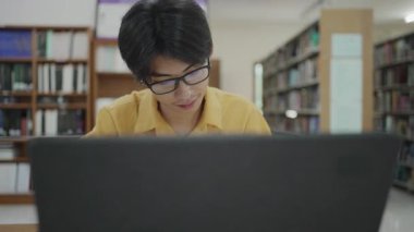 E-öğrenme konsepti. Bilgisayarlı sıradan kıyafet giyen genç Asyalı çocuk not alıyor, internetten ders alıyor.