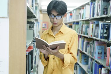 Eğitim, öğrenim ve araştırma için bir kütüphanede kitap okuyan genç bir Asyalı. Okul, üniversite ya da üniversite kampüsünde. Dil ve felsefe öğrenmek için kitap rafında odaklan, kitap ve öğrenci
