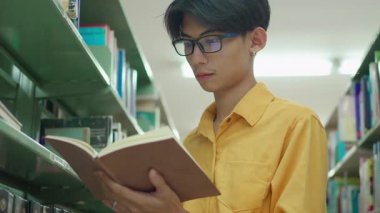 Bir proje için araştırma yapan ya da üniversite kütüphanesinde sınava hazırlanan genç bir erkek öğrenci. Kütüphanede kitap okuyan kendinden emin üniversite öğrencisi.