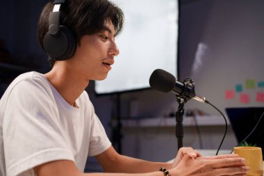 Gülümseyen Asyalı genç radyo sunucuları kulaklıklarla, mikrofonla konuşurken, sohbet ederken, stüdyoda podcast yaparken..