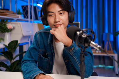 Kulaklık takan genç adam mikrofon kurulumuyla podcast sırasında dikkatle dinliyor.