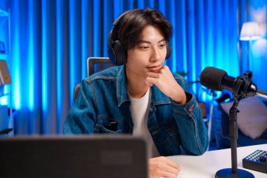 Ev stüdyosunda podcast sunarken kulaklık takan bir adam çenesini dinlendiriyor.