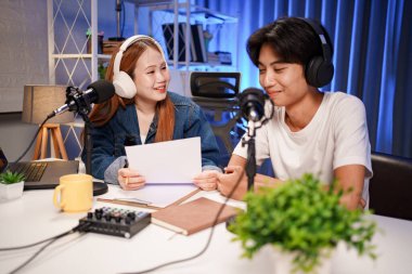 Genç adam ve kadın küçük yayın stüdyosunda mikrofon ve dizüstü bilgisayar kullanarak canlı yayın yapan radyo yayını için röportaj yapacaklar.,