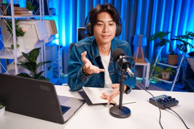 Bilgisayarında kulaklık ve mikroskopla podcast kaydeden bir adam. Parlak stüdyosundan canlı yayın yapan erkek podcaster