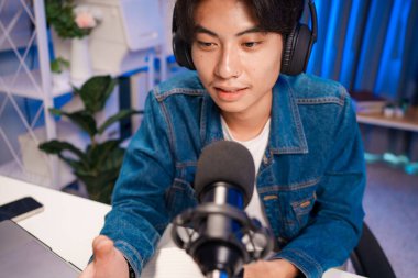 Bilgisayarında kulaklık ve mikroskopla podcast kaydeden bir adam. Parlak stüdyosundan canlı yayın yapan erkek podcaster