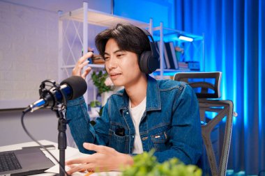 Bilgisayarında kulaklık ve mikroskopla podcast kaydeden bir adam. Parlak stüdyosundan canlı yayın yapan erkek podcaster