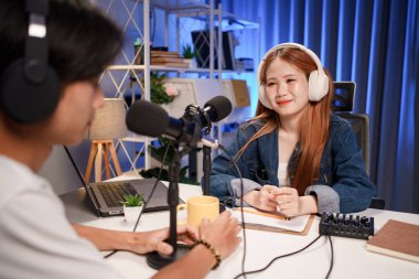 Genç adam ve kadın küçük yayın stüdyosunda mikrofon ve dizüstü bilgisayar kullanarak canlı yayın yapan radyo yayını için röportaj yapacaklar.,