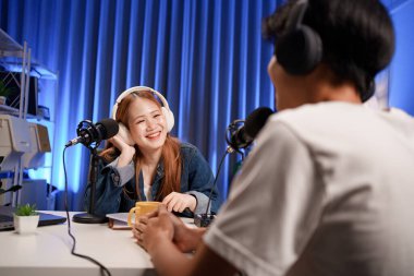 Genç adam ve kadın küçük yayın stüdyosunda mikrofon ve dizüstü bilgisayar kullanarak canlı yayın yapan radyo yayını için röportaj yapacaklar.,